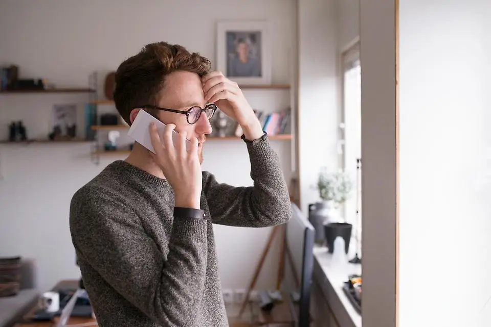 En man som står och pratar i telefon inomhus i hemmamiljö.