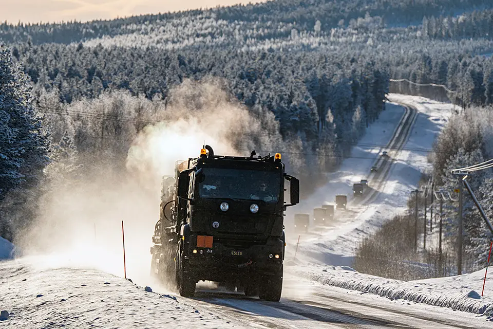 Kolonn med militära lastbilar på väg genom ett vintrigt skogslandskap.