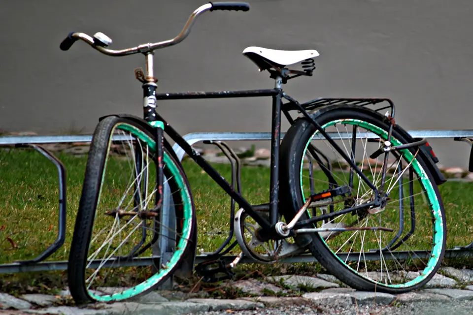 En övergiven och trasig vit cykel, som är fastkedjan vid ett stuprör.